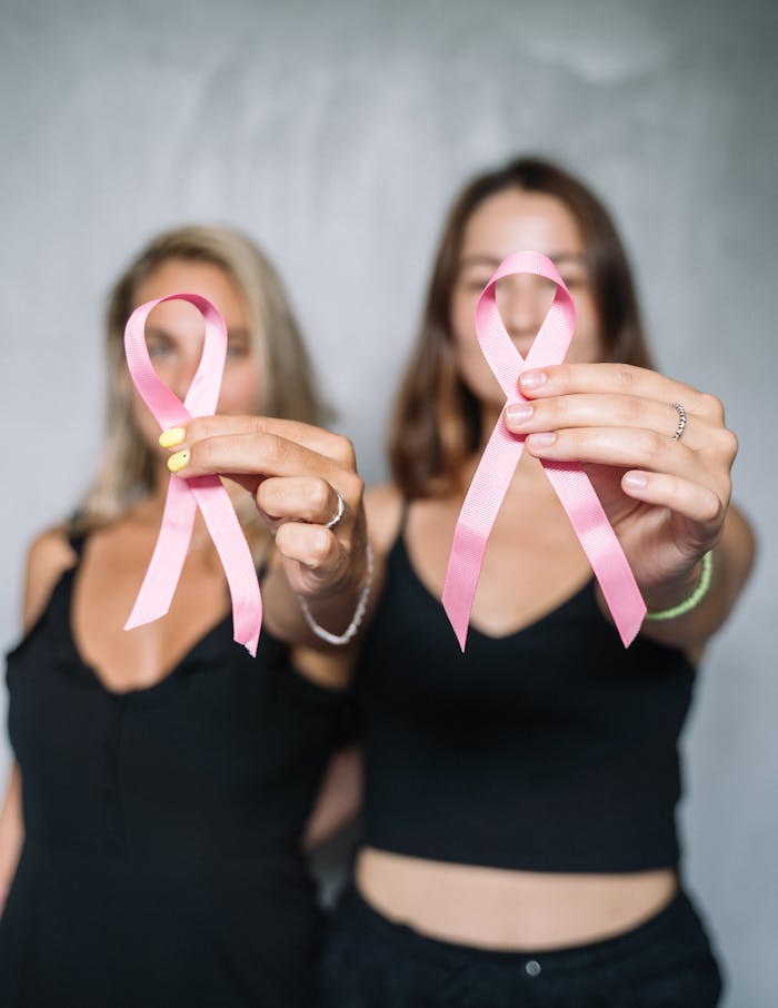 Two women holding pink ribbons, symbolizing breast cancer awareness and support.